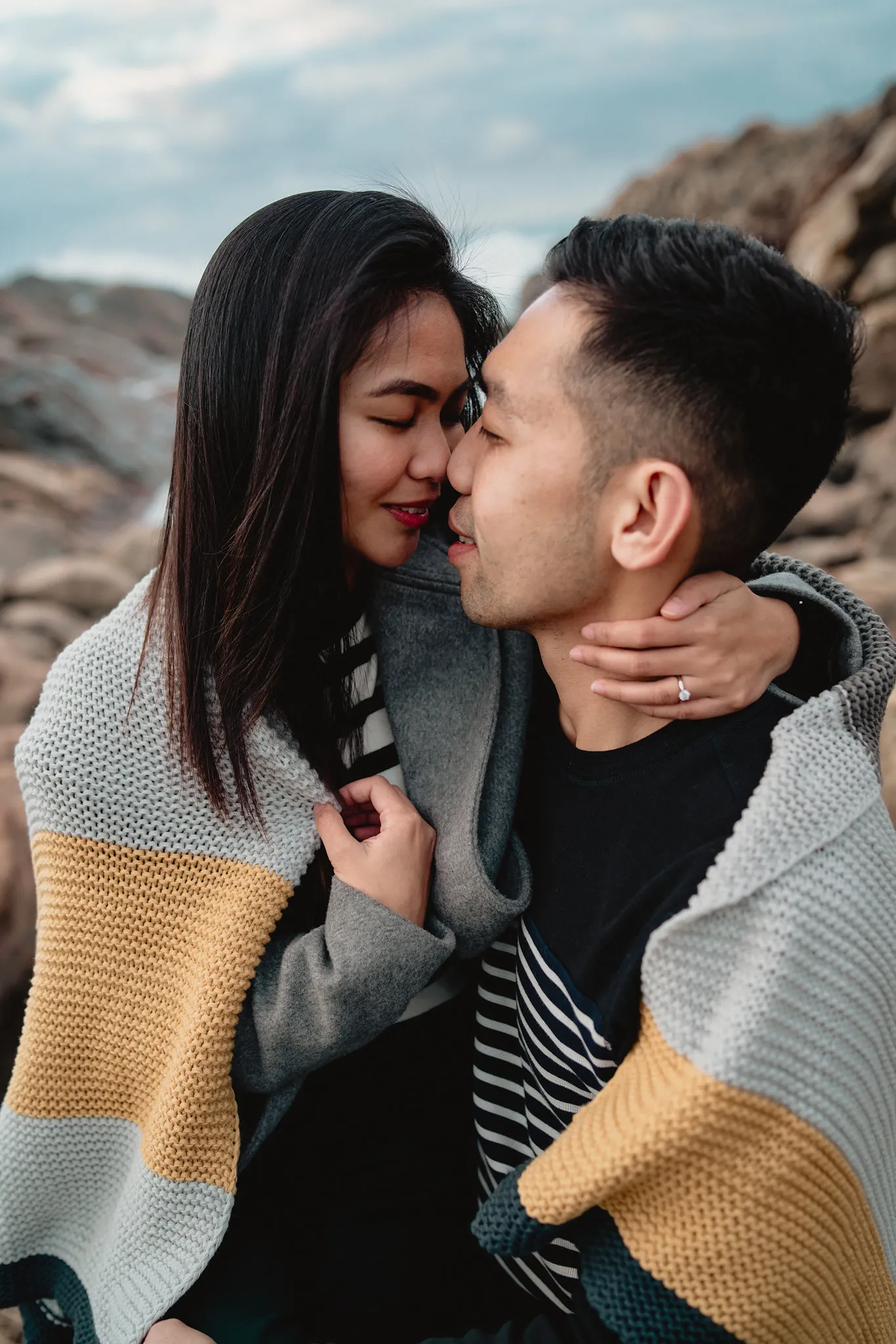 Zaneta and Vryan wrapped in a blanket on the coast, laughing