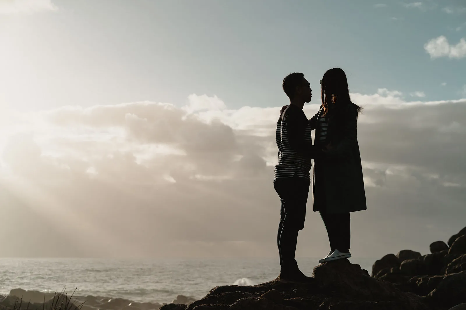 Zaneta and Vryan in silhouette on a rocky headland above the sea