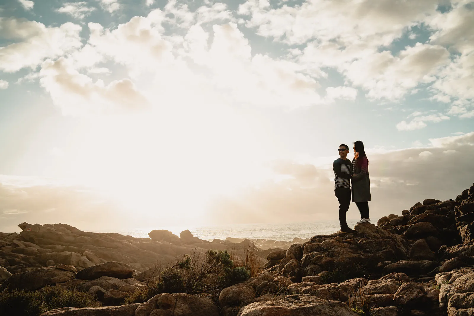 Zaneta and Vryan on the rocks with the sun breaking through the cloud